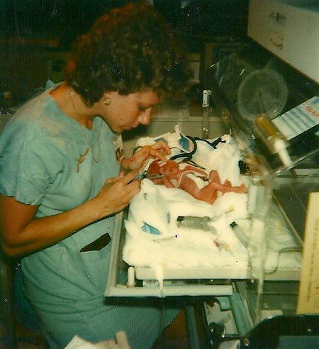 Dr. Bianchi is wearing scrubs and attends to a premature infant in an incubator.