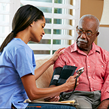 A nurse takes the blood pressure of an elderly man. Both are African-American.