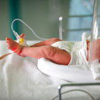 An infant’s feet and torso are visible in a hospital setting.