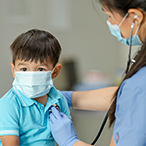 Boy seated while healthcare provider listens to his heart with a stethoscope.