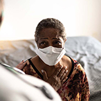 African American woman in healthcare provider’s office wearing a mask and speaking to a provider.