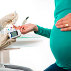 Pregnant person midsection view, holding finger out for diabetes blood test.