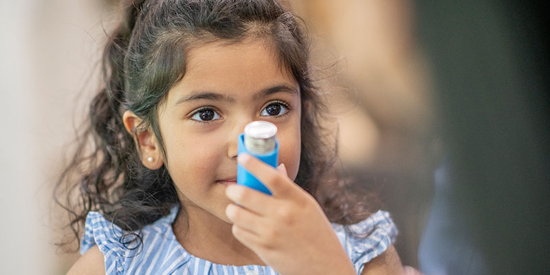 Child holding inhaler for asthma treatment.