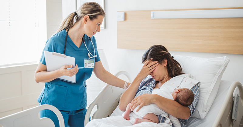 Practitioner at bedside of new parent with hand over eyes, holding newborn.