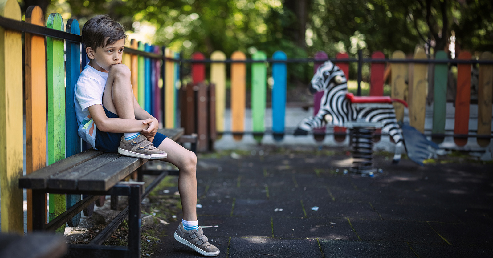 Child sitting alone on a playground bench.