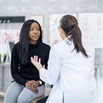 Seated person talking to health care professional in white lab coat.