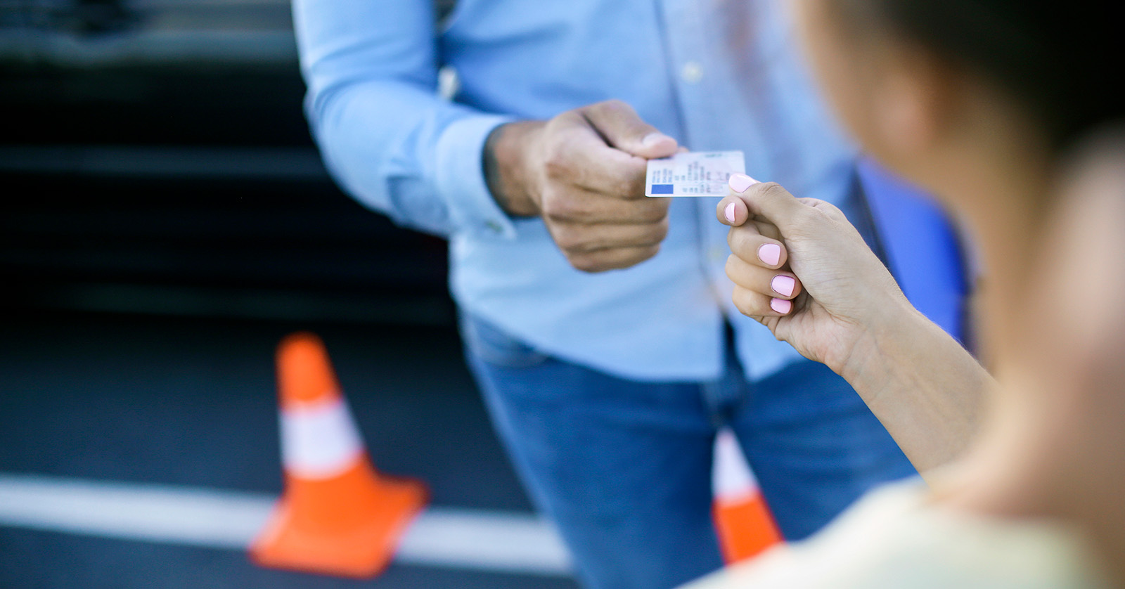 Close up view of older male handing a driver’s license to a younger female.