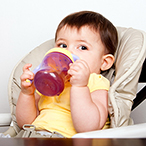 Small child in high chair drinking juice from a sippy cup.