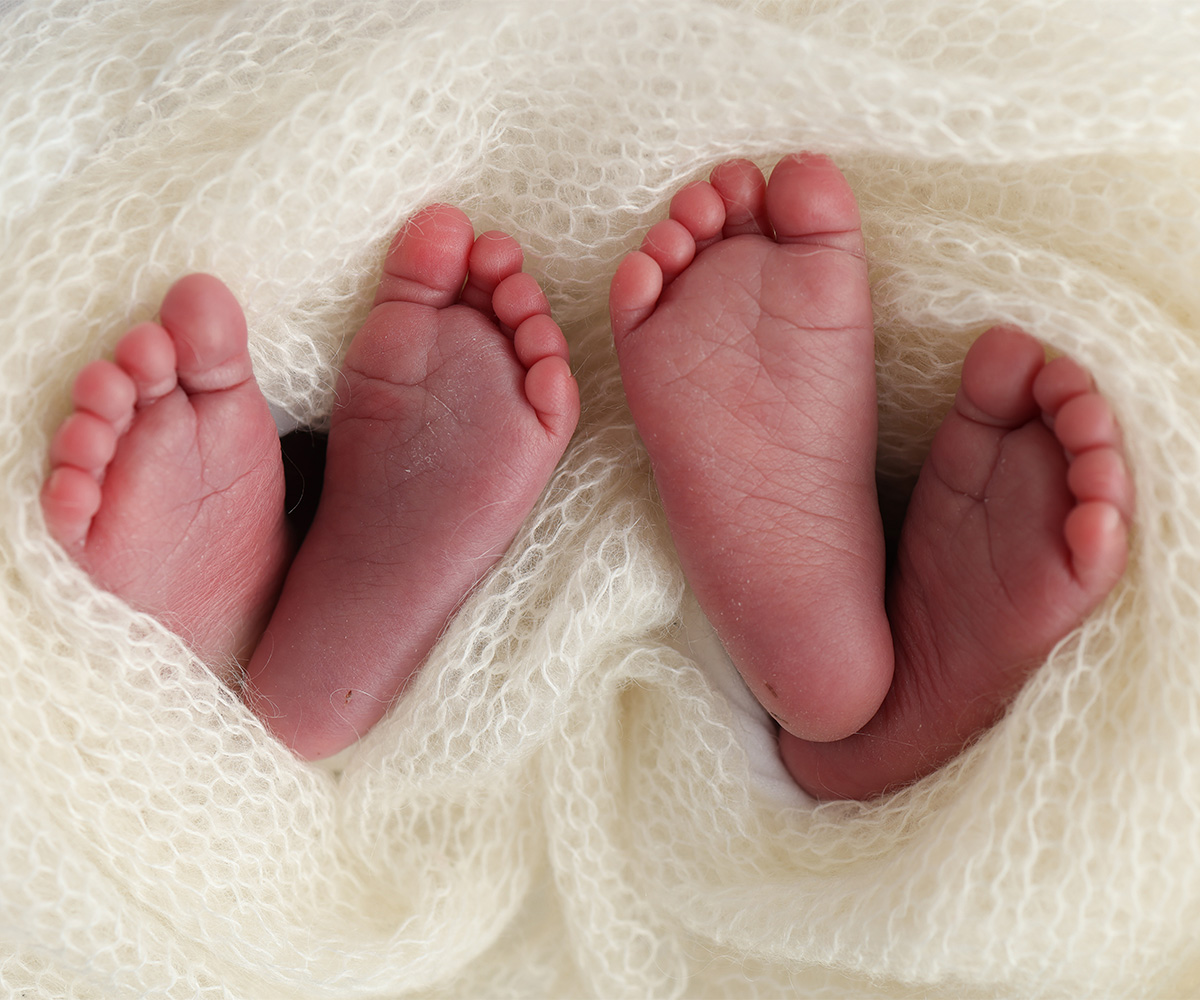 Two pairs of baby feet wrapped in a knitted blanket.
