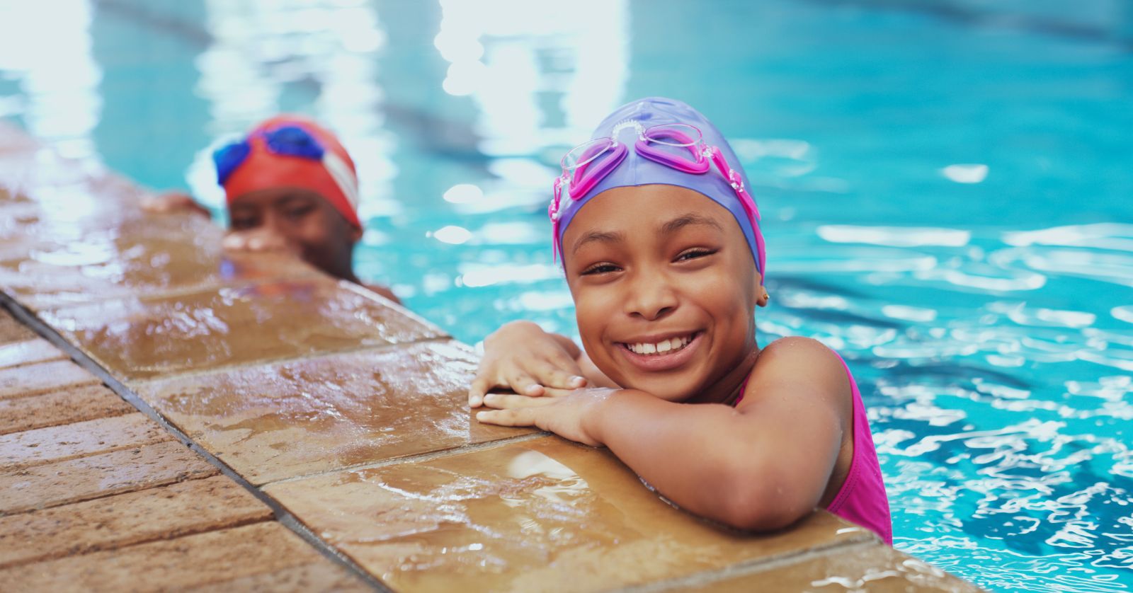 Child in swimming pool, head, neck and arms above water, poised at pool side ledge.