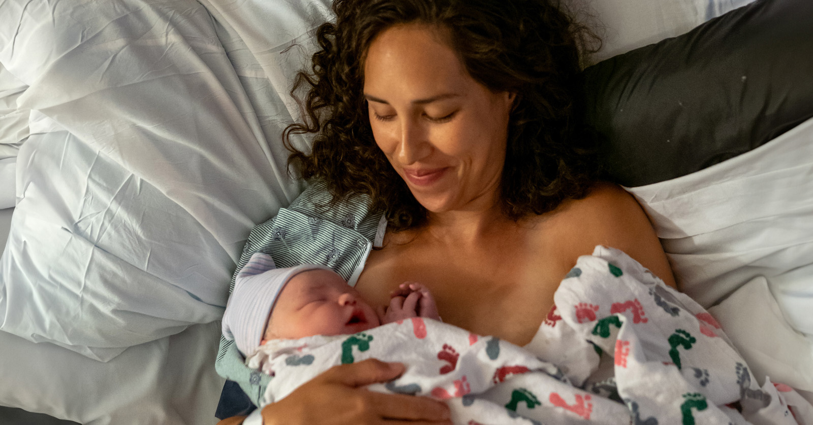 Infant resting on the bare chest of a caregiver under a blanket.