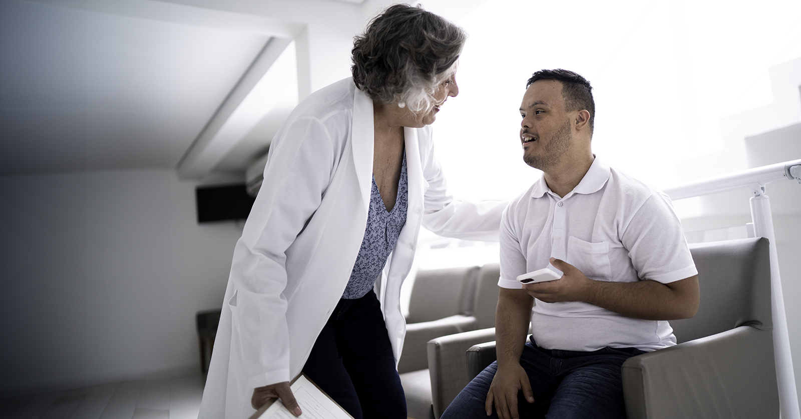 Health care worker with white coat talks to individual with Down syndrome.