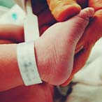 Hand holding infant foot. Hospital paper band is visible on infant’s ankle.