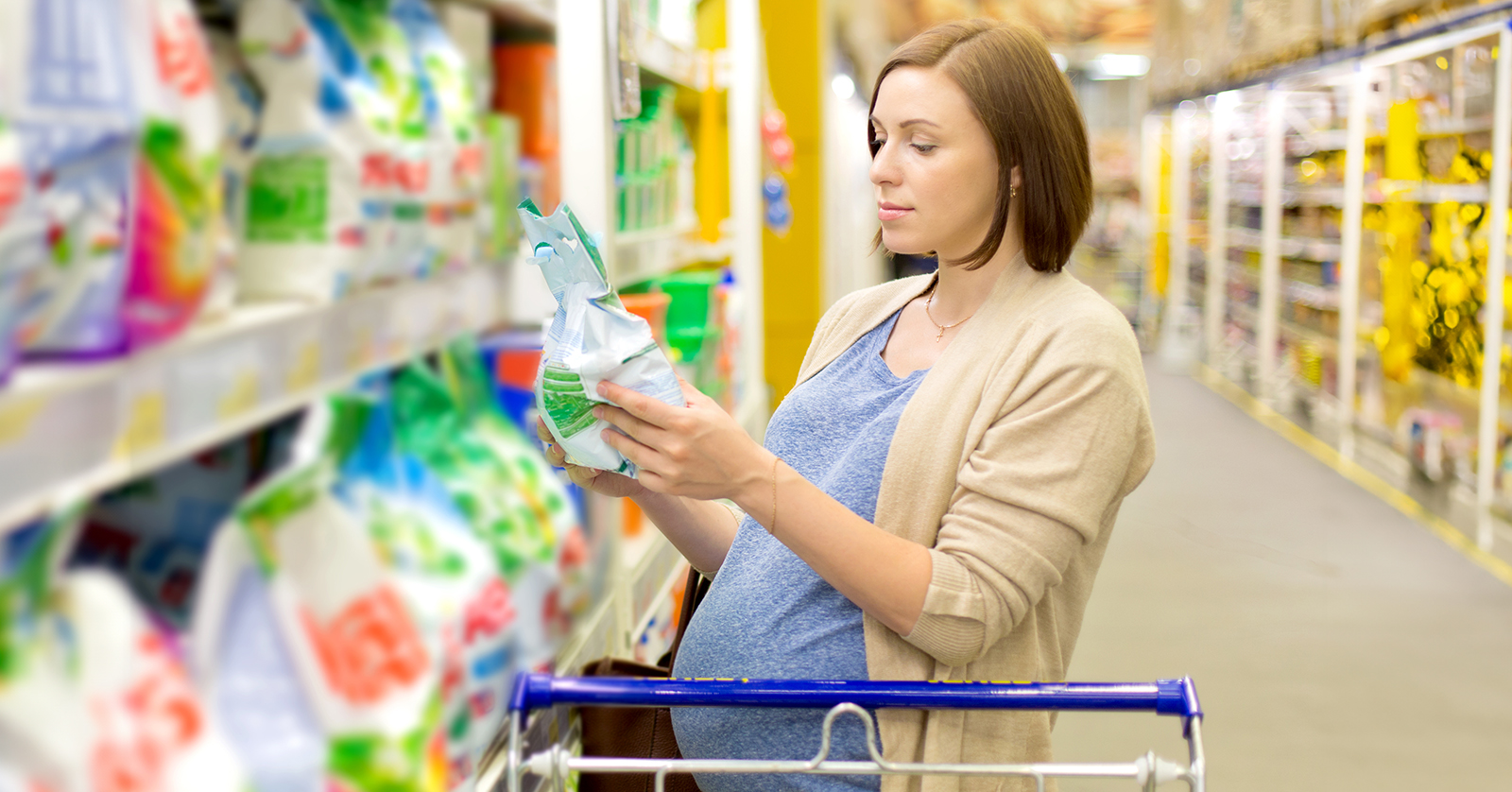 Pregnant person behind a shopping cart reading a package label.