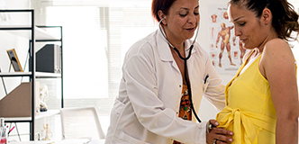 A health care worker listens to a pregnant person’s abdomen with a stethoscope.