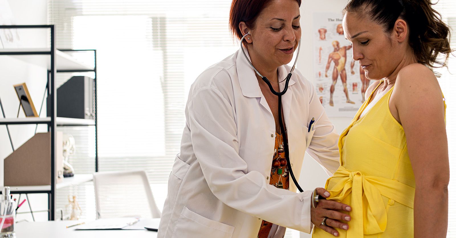 A health care worker listens to a pregnant person’s abdomen with a stethoscope.