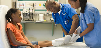 Child seated on gurney while providers adjust cast on her lower leg.