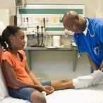 Child seated on gurney while providers adjust cast on her lower leg.