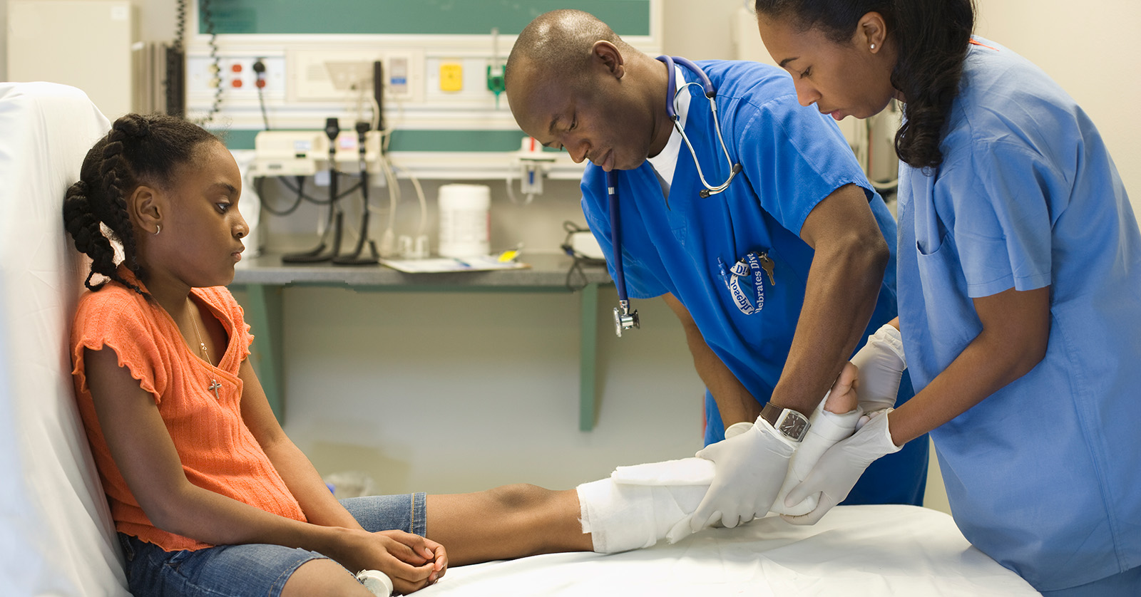 Child seated on gurney while providers adjust cast on her lower leg.