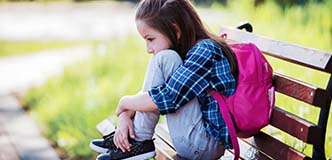 Child sitting on bench, hunched, holding knees.