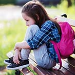 Child sitting on bench, hunched, holding knees.