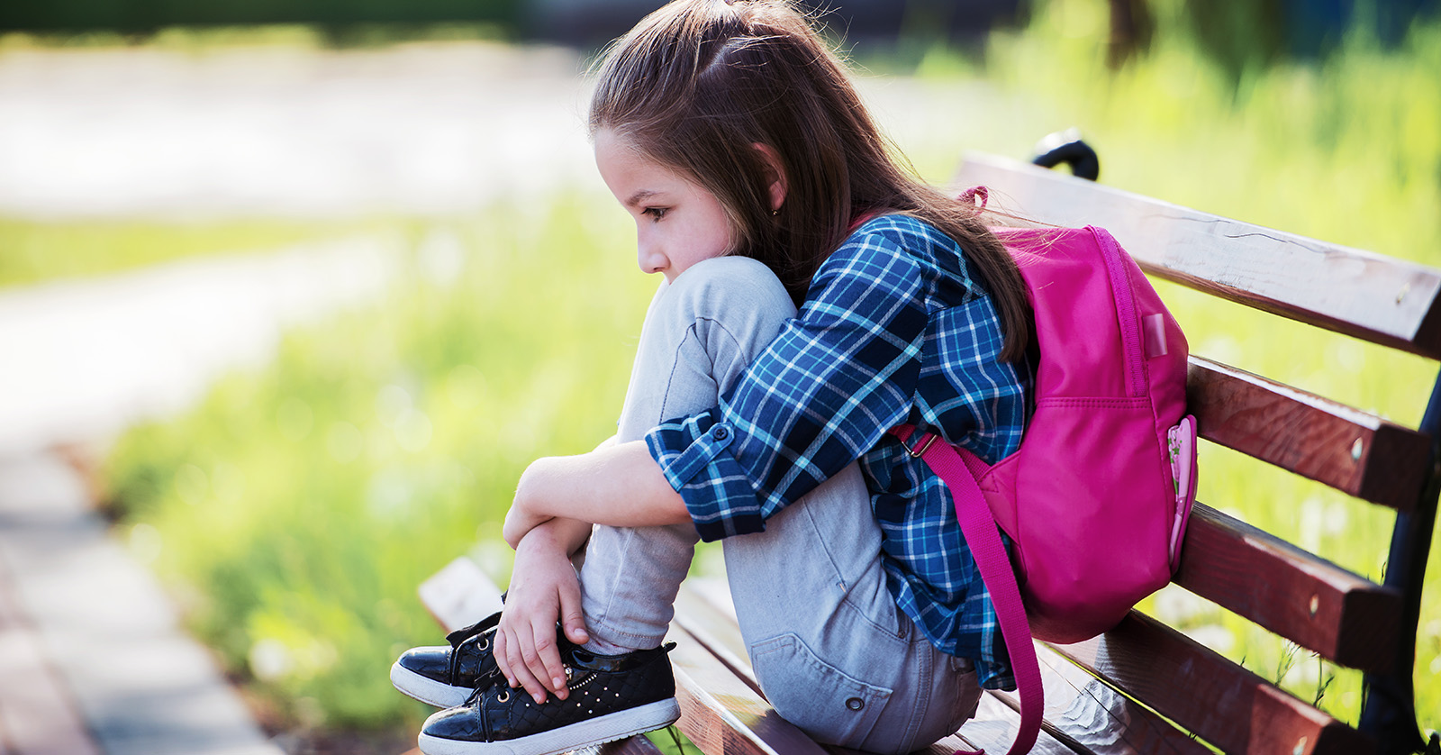 Child sitting on bench, hunched, holding knees.