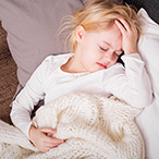 Child laying on couch with hand on forehead.