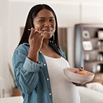 Smiling pregnant person eating a bowl of multicolored fruit.