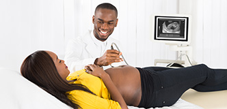 Technician passes scanner over abdomen of pregnant person lying on examination table.