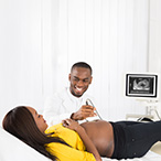 Technician passes scanner over abdomen of pregnant person lying on examination table.