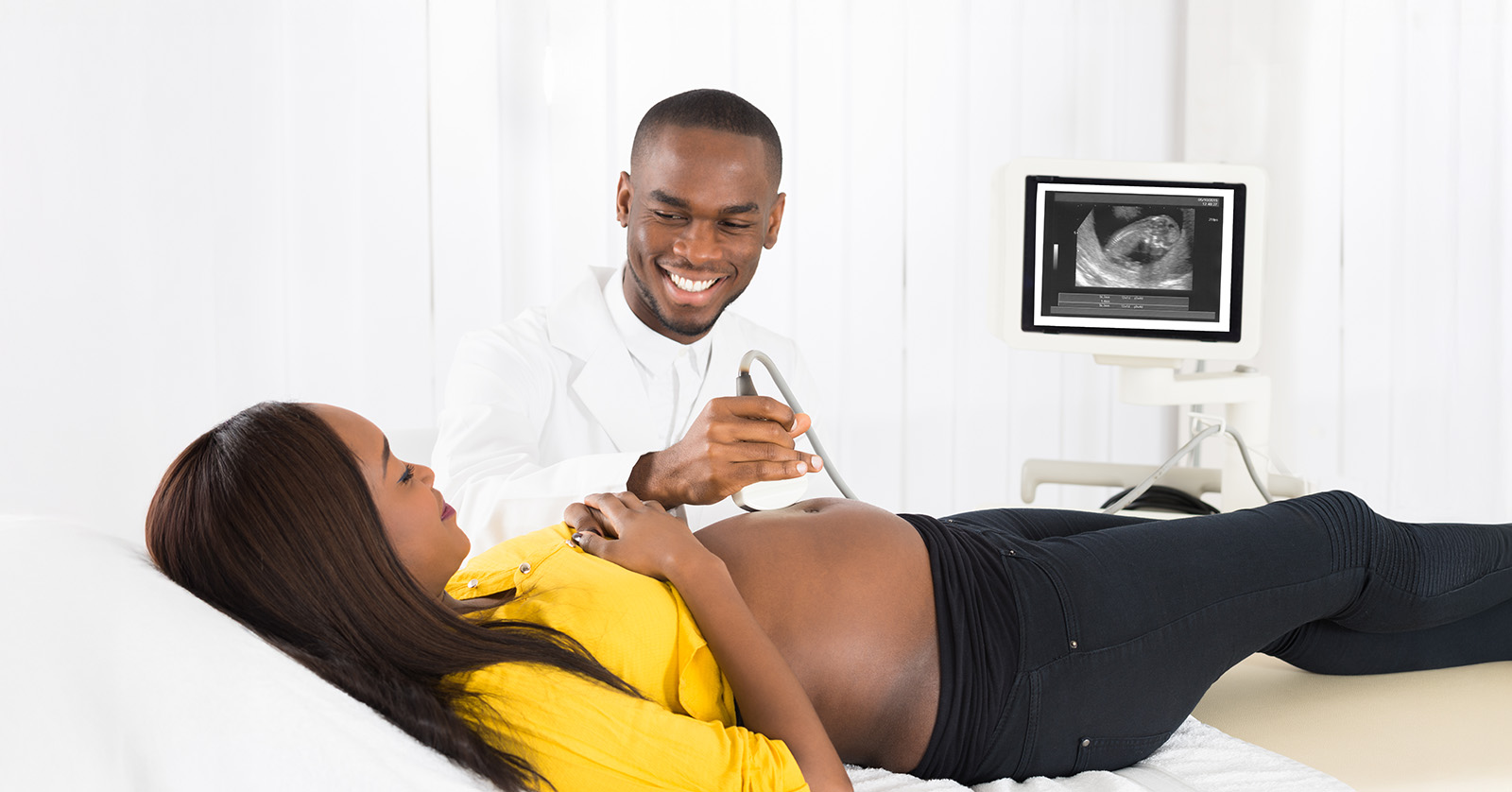 Technician passes scanner over abdomen of pregnant person lying on examination table.