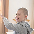 A boy with Down syndrome gives his mother a high five. Text overlay: “Drive Down Syndrome Research With Your Unique Story”.