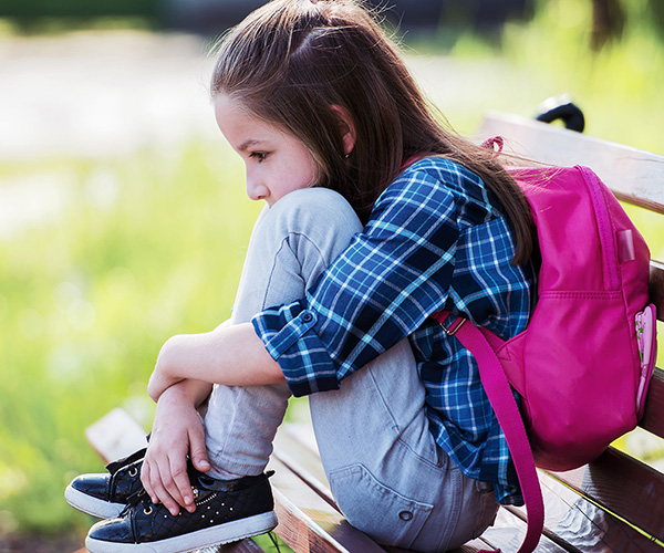 Girl sitting on bench, hunched, holding knees.