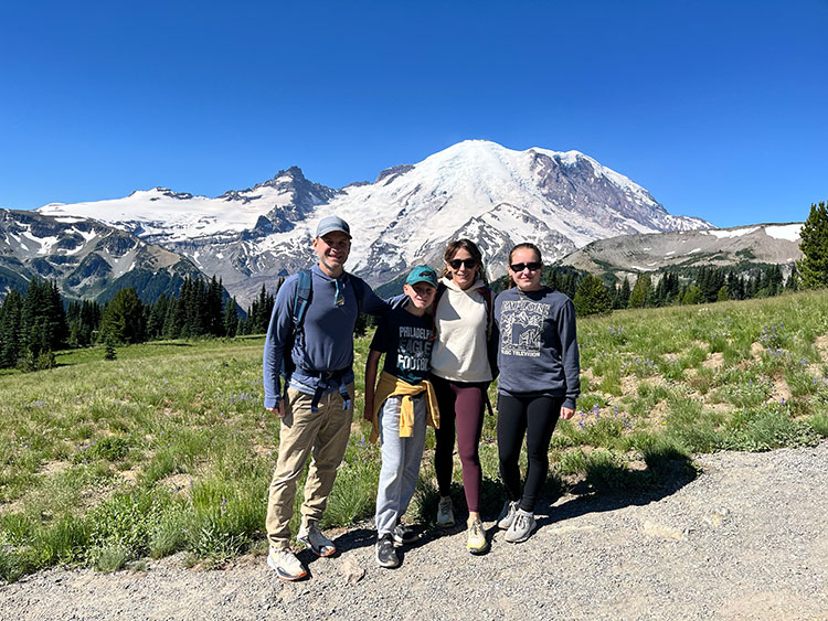 Two adults and two children standing in front of a snowy mountain.