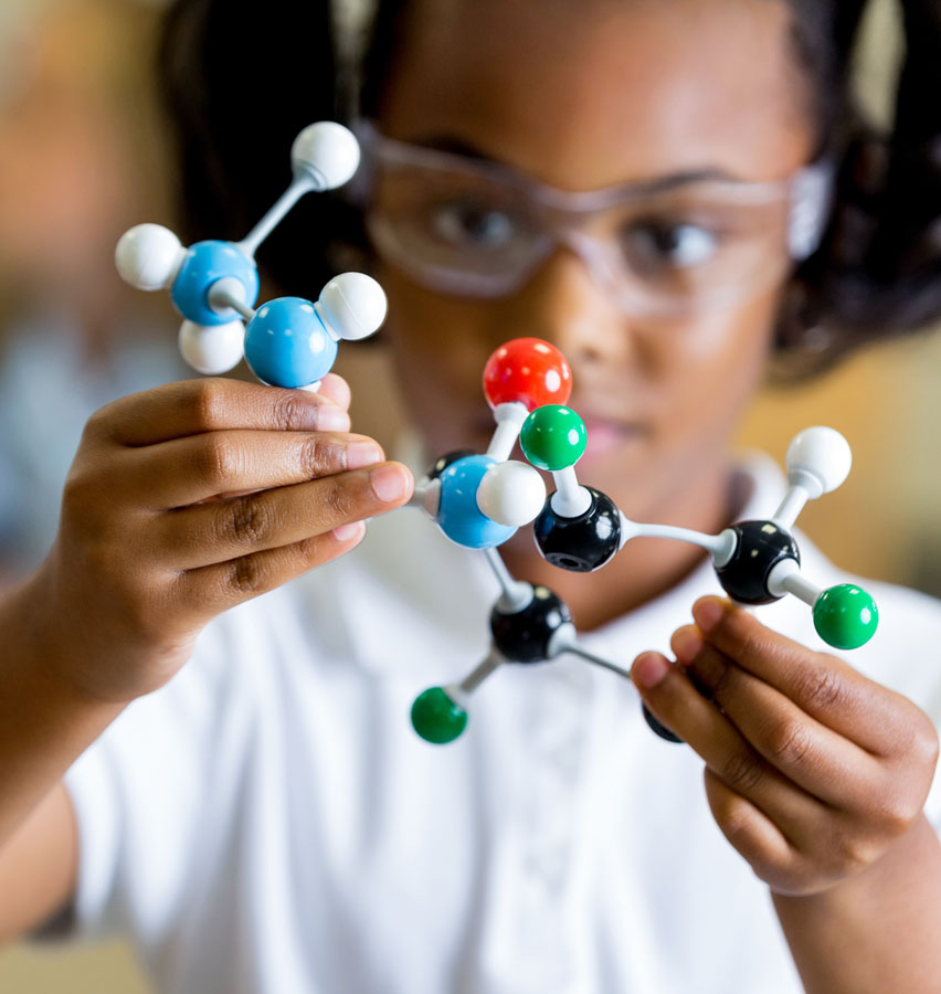 A young girl wearing lab goggles and holding a molecular model.