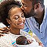 A man kisses a woman on the forehead as she smiles down at the baby she holds in her arms.